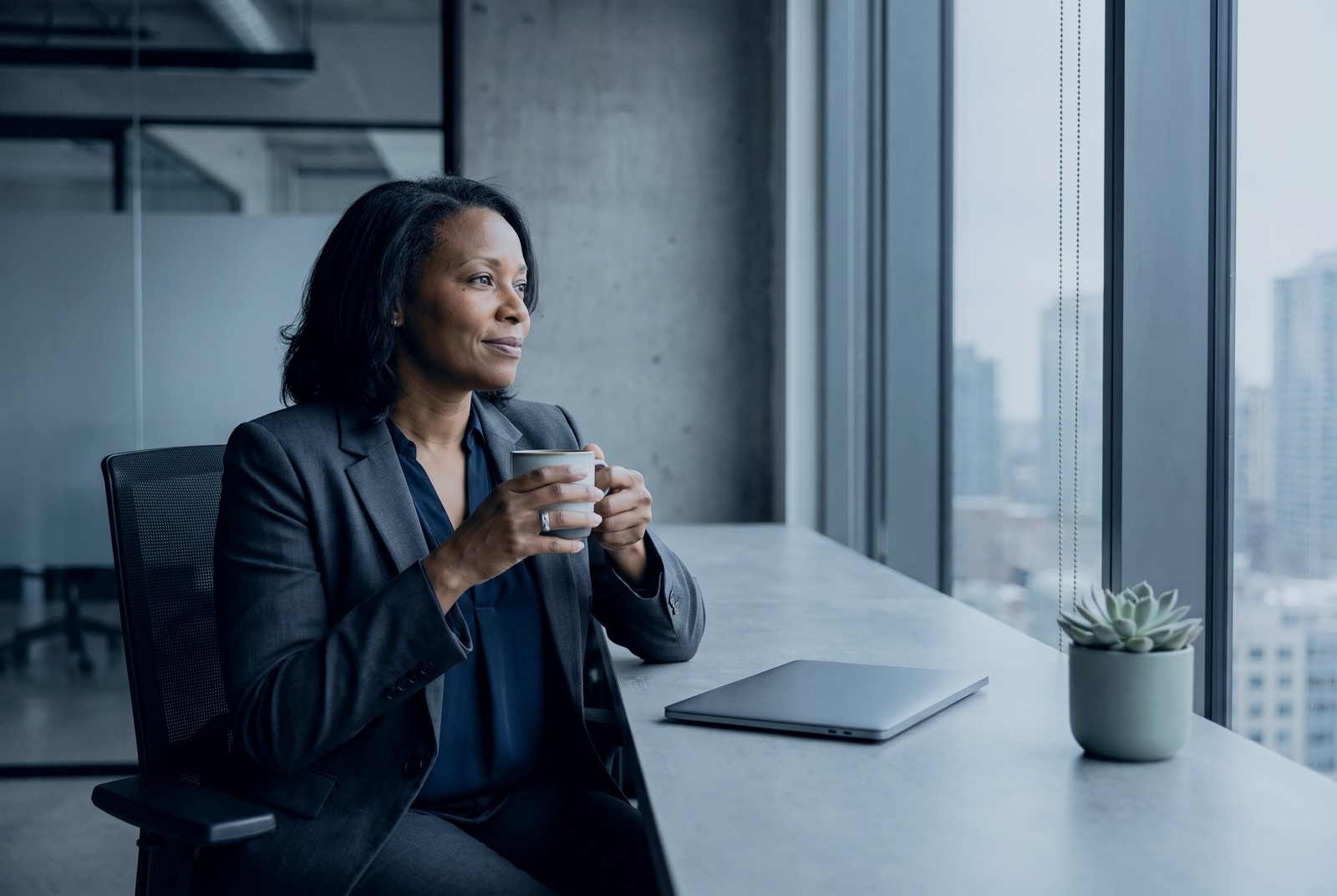 An operations executive with a coffee by an office window, at ease at the start of the week